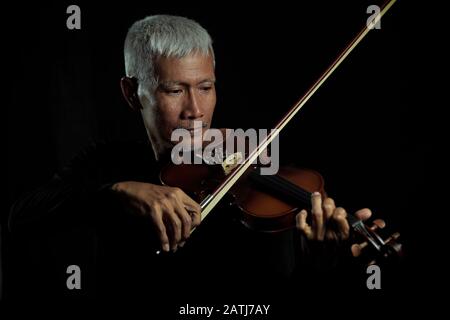 Der ältere Mann spielt Geige und genießt Musik auf schwarz isoliertem Hintergrundporträt Stockfoto