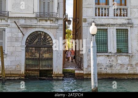 Eine Gruppe von Touristen, die auf einer schmalen Durchfahrt spazieren, die direkt zum Canal Grande in Venedig, Italien führt Stockfoto