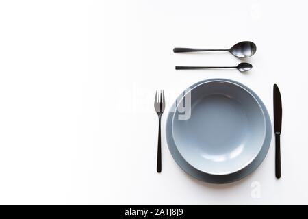 Teller mit schwarzer Gabel, Löffel, Dessertlöffel und einem Messer isoliert auf weißem Studiohintergrund. Kopierbereich Stockfoto