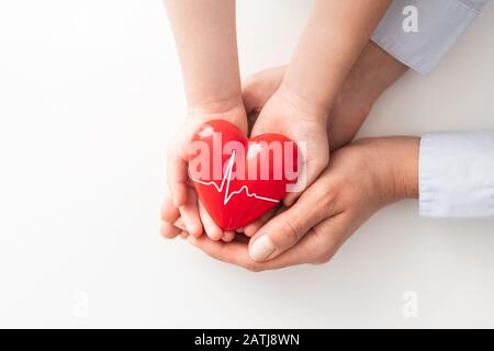 Ein Erwachsener, eine Mutter und ein Kind halten ein rotes Herz in den Händen. Konzept für Wohltätigkeitsorganisation, Krankenversicherung, Liebe, internationaler Kardiologietag. Stockfoto