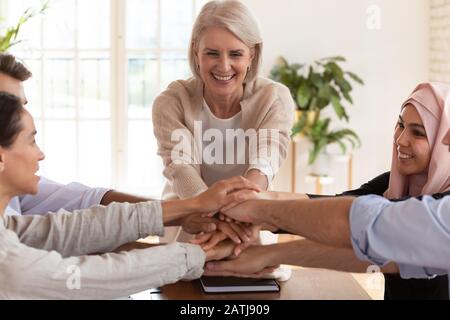 Lächelnde multiethnische Kollegen stapeln Hände, die bei Treffen Einheit zeigen Stockfoto