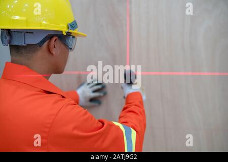 Der Techniker arbeitet daran, die Wand mit einem elektrischen Bohrer entsprechend dem Markierungspunkt der Laser-Füllstandsmaschine zu bohren Stockfoto