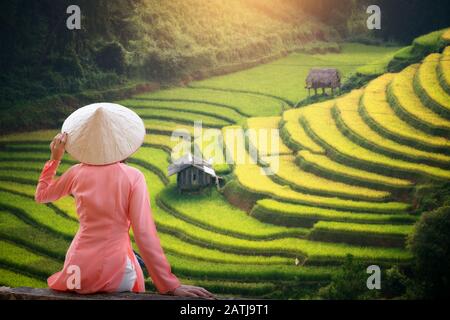 Touristin trägt Ao Dai Vietnam traditionelles Kleid sitzend Reisterterrasse schöne Landschaft in Mu Cang Chai Vietnam. Stockfoto