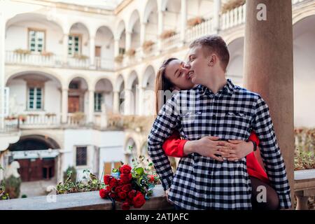 Romantisches Datum am Valentinstag. Frau küsst Freund auf Wange. Ein Paar umarmte sich im italienischen Hof in Lemberg mit Rosen Stockfoto