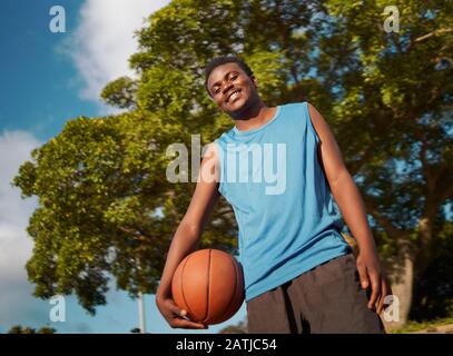 Niedriger Blickwinkel eines selbstbewussten männlichen Basketballspielers, der den Ball in der Hand hält und zur Kamera blickt Stockfoto