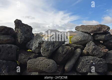 Vulkanische Steinwand mit verschwommenem Vulkan im Hintergrund. Lanzarote, Spanien. Stockfoto