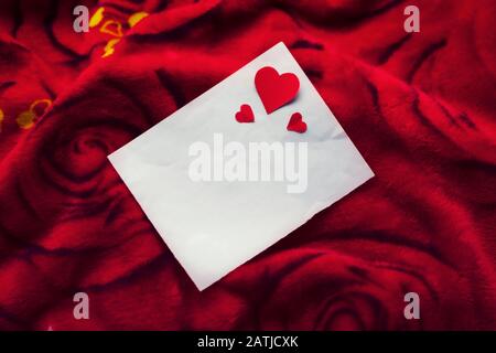 Leere weiße Karte oder Papier mit kleinen Herzen auf rotem Rosen-Blumenhintergrund mit Kopierbereich. Konzept für Banner, valentinstag Angebot, Verkauf, p Stockfoto
