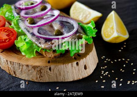 Appetitliches Smorrebrod mit norwegischem Hering, Salat, blauer Zwiebel, Zitrone und Tomate liegt auf einem Holzbrett Stockfoto