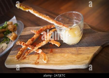 Leckere Knisterstreifen aus Schweinefleisch und eine apfelsoße tauchen in ein Glas auf einem Holzbrett, das als Snack oder Vorspeise serviert wird Stockfoto