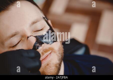 Spa Gesichtshautpflege für Männer, Entfernen der schwarzen Holzkohlemaske aus der Nase im Barbershop Stockfoto