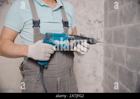 Bauherr mit pneumatischem Schlagbohr-Perforator mit Rautenkrone, das Loch in der Wand für Elektrokabel, Steckdose, Schalter macht Stockfoto