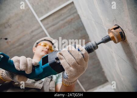 Bauarbeiter pneumatische Hammerbohrer Bohrung in Betonziegelwand mit Rautenkrone für Elektrokabel, Steckdose, Schalter Stockfoto