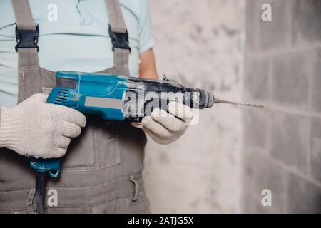 Bauherr mit pneumatischem Schlagbohr-Perforator mit Rautenkrone, das Loch in der Wand für Elektrokabel, Steckdose, Schalter macht Stockfoto