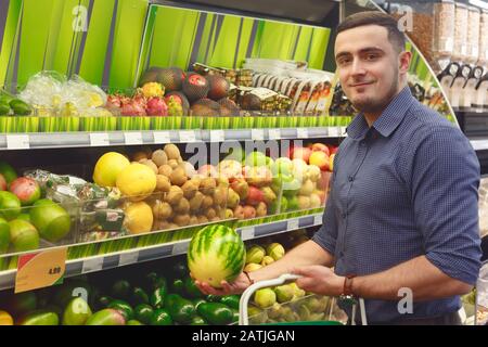 Junge Mann wählen, um Zwergwassermelone im Supermarkt oder Lebensmittelgeschäft zu kaufen Stockfoto