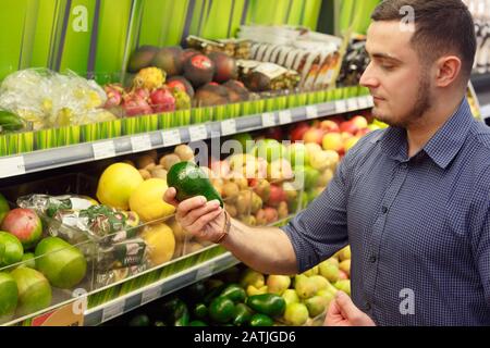 Junger Mann Kunde wählt Avocados im Supermarkt Stockfoto
