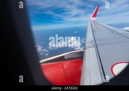 Blick aus dem AIRBUS-FLUGFENSTER A320 an einem sonnigen Tag mit Blick auf den Flügel mit roter Firmentageband, sonnigem Himmel und Wolken Stockfoto