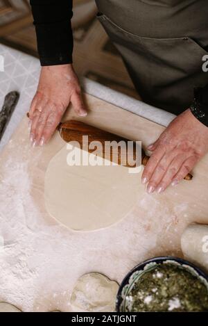 Eine Erwachsene Frau rollt Teig in ihrer Küche, um Backen oder Knödel zuzubereiten, Manti. Stockfoto
