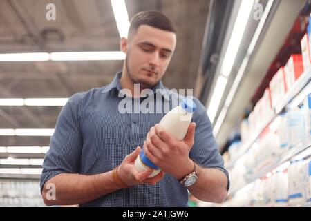 Ein Mann las in der Milchabteilung des Supermarktes eine Flasche mit Milch oder Joghurt. Ein Mann kauft Milchprodukte im Laden Stockfoto