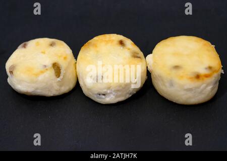 Drei runde Käsekuchen mit Rosinen auf schwarzem Brett. Hausgemachte Käsekuchen auf schwarzem Hintergrund. Leckeres kalorienarmes gesundes Dessert aus Cottage chee Stockfoto