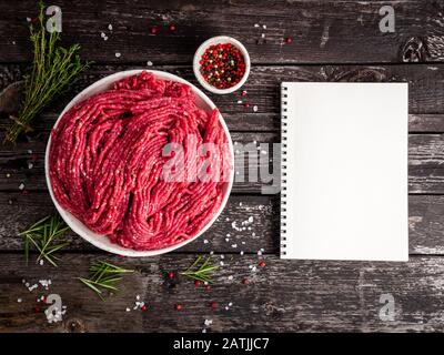 Hackfleisch, gemahlenes Fleisch mit Zutaten zum Kochen auf altem grauem, dunklem Holztisch, Notizblock, Rezept-Mock-up, Draufsicht, Kopierraum Stockfoto