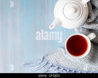 Tee, Teekanne, Kopierer, warmer Strickschal auf blauem Holzhintergrund, gemütliches Haus, Draufsicht Stockfoto