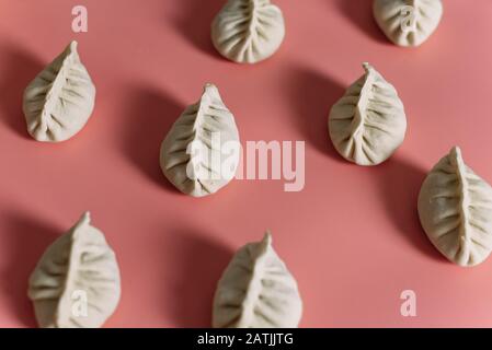 Halbfertigprodukte auf pinkfarbenem Hintergrund. Draufsicht auf Manti oder Knödel. Muster. Stockfoto