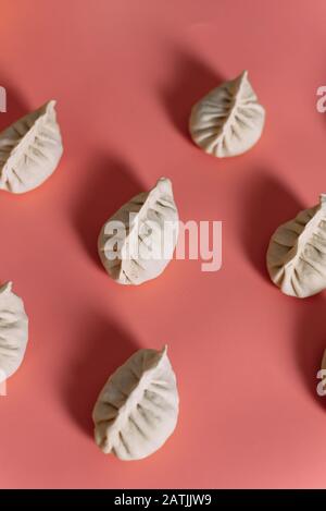 Halbfertigprodukte auf pinkfarbenem Hintergrund. Draufsicht auf Manti oder Knödel. Muster. Stockfoto