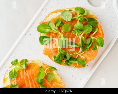 Zwei offene Sandwiches mit Lachs, Frischkäse, Gurkenscheiben auf weißem Marmortisch Stockfoto