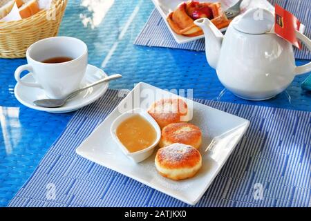 Käsekuchen mit Honig in einem Restaurant. Traditionelle hausgemachte Käsebäckchen oder Kerbbrüter verzierten pulverförmigen Zucker in der Platte in der Nähe. Hea Stockfoto