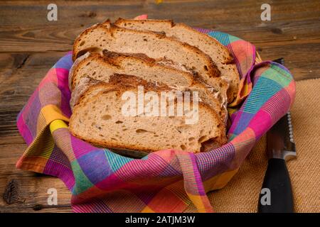 Frisch geschnittenes Brot in einem Brotkorb aus Jutestoff auf rustikalem Holzhintergrund. Stockfoto