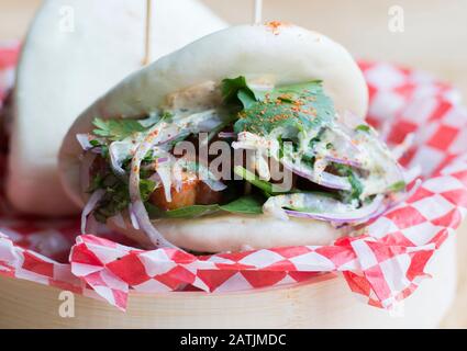 Bao-Brötchen mit Schweinebauch und Roccato-Sauce werden mit einem blauen Teller in einem Restaurant gezeigt Stockfoto