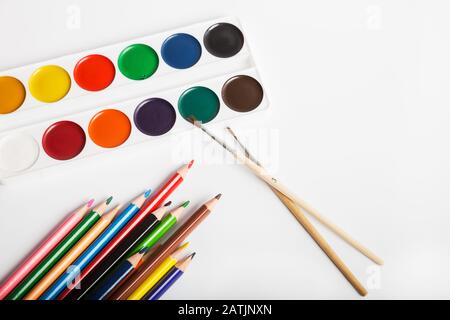 Set mit Aquarellfarben mit Pinsel und Farbstiften zum Zeichnen auf weißem Hintergrund Stockfoto