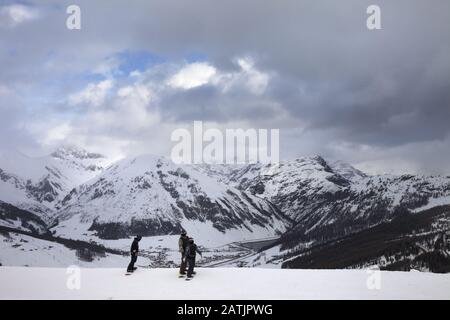 Die Gruppe der Snowboarder startet auf Abfahrt. Hohe Schneeberge und bewölkter Sturmhimmel im Winter vor blizzard. Skigebiet Mottolino Fun Mountai Stockfoto