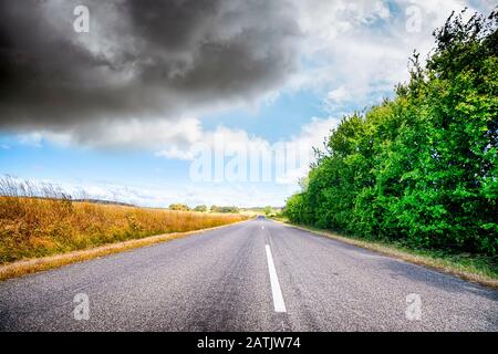 Asphaltstraße in ländlicher Landschaft mit lebhaften Farben unter bewölktem Himmel Stockfoto