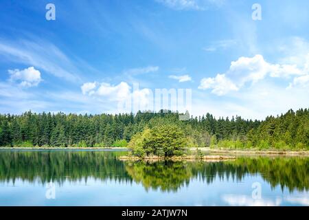 Bunte Seenlandschaft mit Baumreflexionen im Wasser und einer kleinen Insel in der Mitte Stockfoto