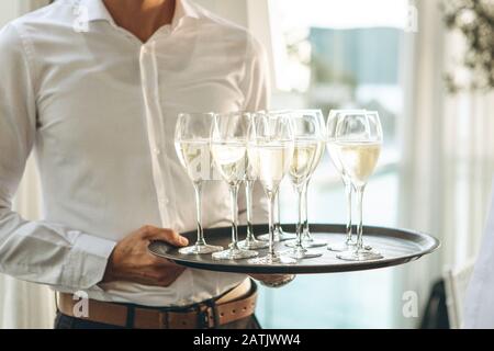 Der Kellner hält ein Tablett mit Gläsern Champagner oder weißem Sekt. Service im Restaurant. Stockfoto