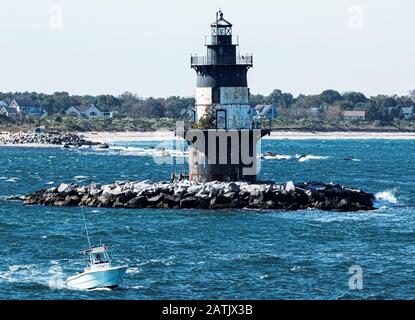 An einem windigen Tag mit rauer See und dem Strand im Hintergrund passiert ein Boot den Orient Point Lighthouse. Stockfoto