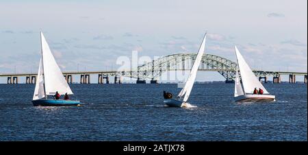 Drei zweiköpfige Segelboote, die auf einem windigen Dezember 2019 Nachmittag im Wasser der großen Südbucht mit der Fire Island Bridge im Backgrou segeln Stockfoto