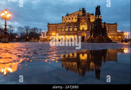 Dresden, Deutschland. Februar 2020. Das Semper-Opernhaus und das König-Johann-Denkmal spiegeln sich am Abend in einer Pfütze auf dem Theaterplatz wider. Kredit: Robert Michael / dpa-Zentralbild / dpa / Alamy Live News Stockfoto