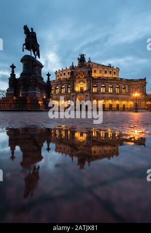 Dresden, Deutschland. Februar 2020. Das Semper-Opernhaus und das König-Johann-Denkmal spiegeln sich am Abend in einer Pfütze auf dem Theaterplatz wider. Kredit: Robert Michael / dpa-Zentralbild / dpa / Alamy Live News Stockfoto