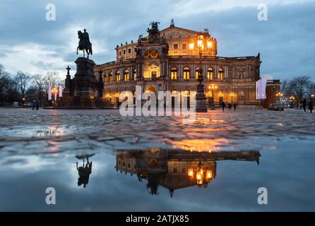 Dresden, Deutschland. Februar 2020. Das Semper-Opernhaus und das König-Johann-Denkmal spiegeln sich am Abend in einer Pfütze auf dem Theaterplatz wider. Kredit: Robert Michael / dpa-Zentralbild / dpa / Alamy Live News Stockfoto