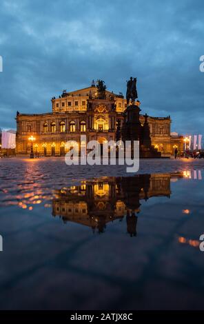 Dresden, Deutschland. Februar 2020. Das Semper-Opernhaus und das König-Johann-Denkmal spiegeln sich am Abend in einer Pfütze auf dem Theaterplatz wider. Kredit: Robert Michael / dpa-Zentralbild / dpa / Alamy Live News Stockfoto