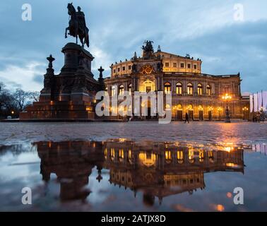 Dresden, Deutschland. Februar 2020. Das Semper-Opernhaus und das König-Johann-Denkmal spiegeln sich am Abend in einer Pfütze auf dem Theaterplatz wider. Kredit: Robert Michael / dpa-Zentralbild / dpa / Alamy Live News Stockfoto