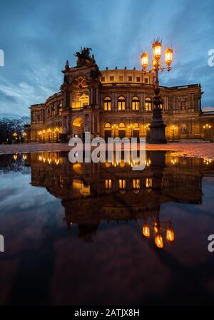 Dresden, Deutschland. Februar 2020. Das Semper-Opernhaus spiegelt sich abends in einer Pfütze auf dem Theaterplatz wider. Kredit: Robert Michael / dpa-Zentralbild / dpa / Alamy Live News Stockfoto