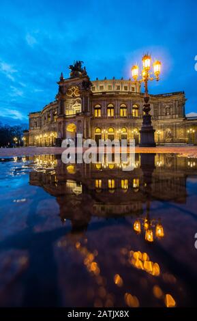 Dresden, Deutschland. Februar 2020. Das Semper-Opernhaus spiegelt sich abends in einer Pfütze auf dem Theaterplatz wider. Kredit: Robert Michael / dpa-Zentralbild / dpa / Alamy Live News Stockfoto