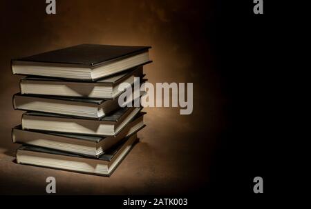 Stapel von Hardcover-Büchern auf braunem Hintergrund, Platz für Text auf der rechten Seite Stockfoto