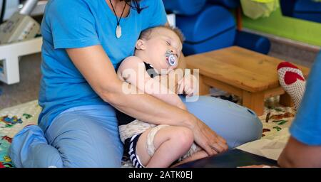 Portrait eines müden Babys mit zerebraler Lähmung über die Physiotherapie in einem Rehabilitationszentrum. Ein behinderter Junge hat eine Therapie, indem er Übungen macht. Exhaus Stockfoto