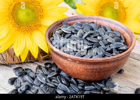 Gelbe Sonnenblumen und Sonnenblumensamen in der Schüssel auf Holzgrund. Nahaufnahme. Stockfoto