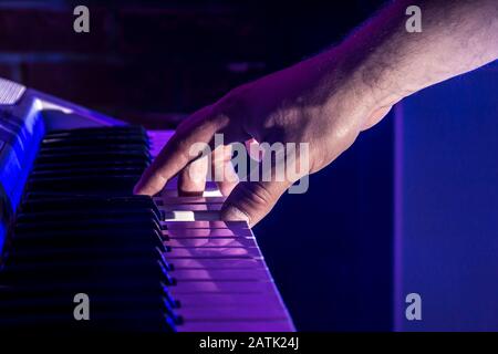 Eine Nahaufnahme der Konzertszene mit der Hand eines männlichen Musikers, der einen Akkord auf einem Synthesizer-Keyboard in blauen Scheinwerfern mit Kopierraum spielt Stockfoto