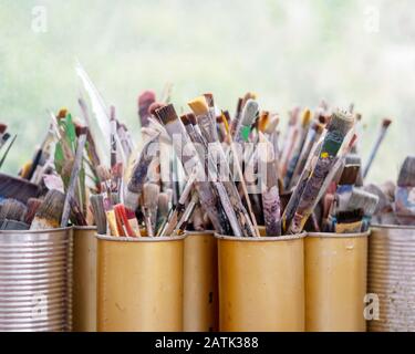 Viele gebrauchte, bunte Künstlerbürsten in verschiedenen Größen werden in verschiedenen Metallboxen gesammelt und aufbewahrt, Kopierraum. Stockfoto